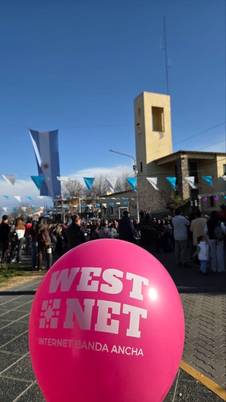 Globo de Westnet en primer plano, con una multitud y la bandera argentina de fondo en un acto de Vendimia